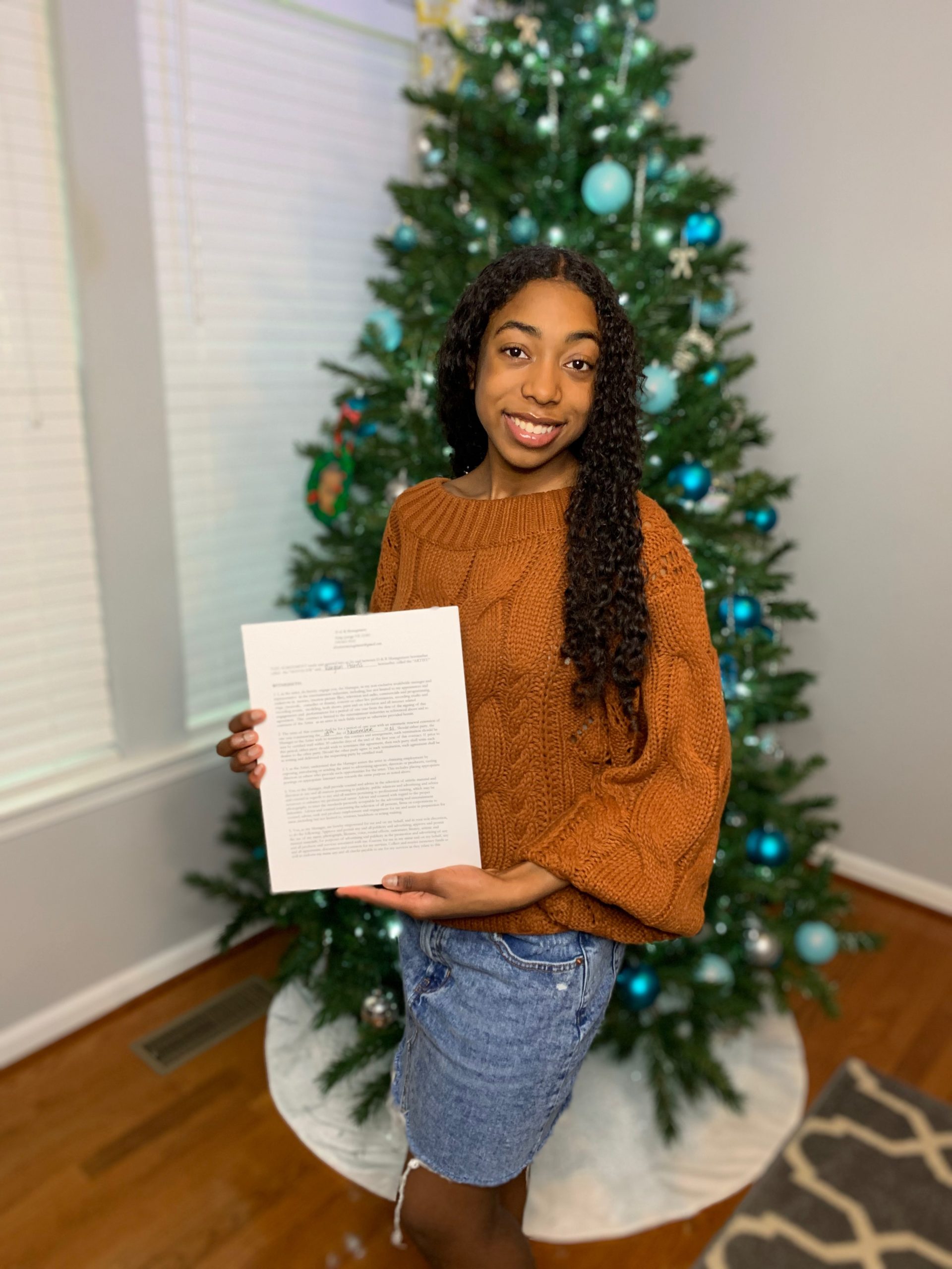 Regan Posing With Her Talent Contract In Front Of A Christmas Tree